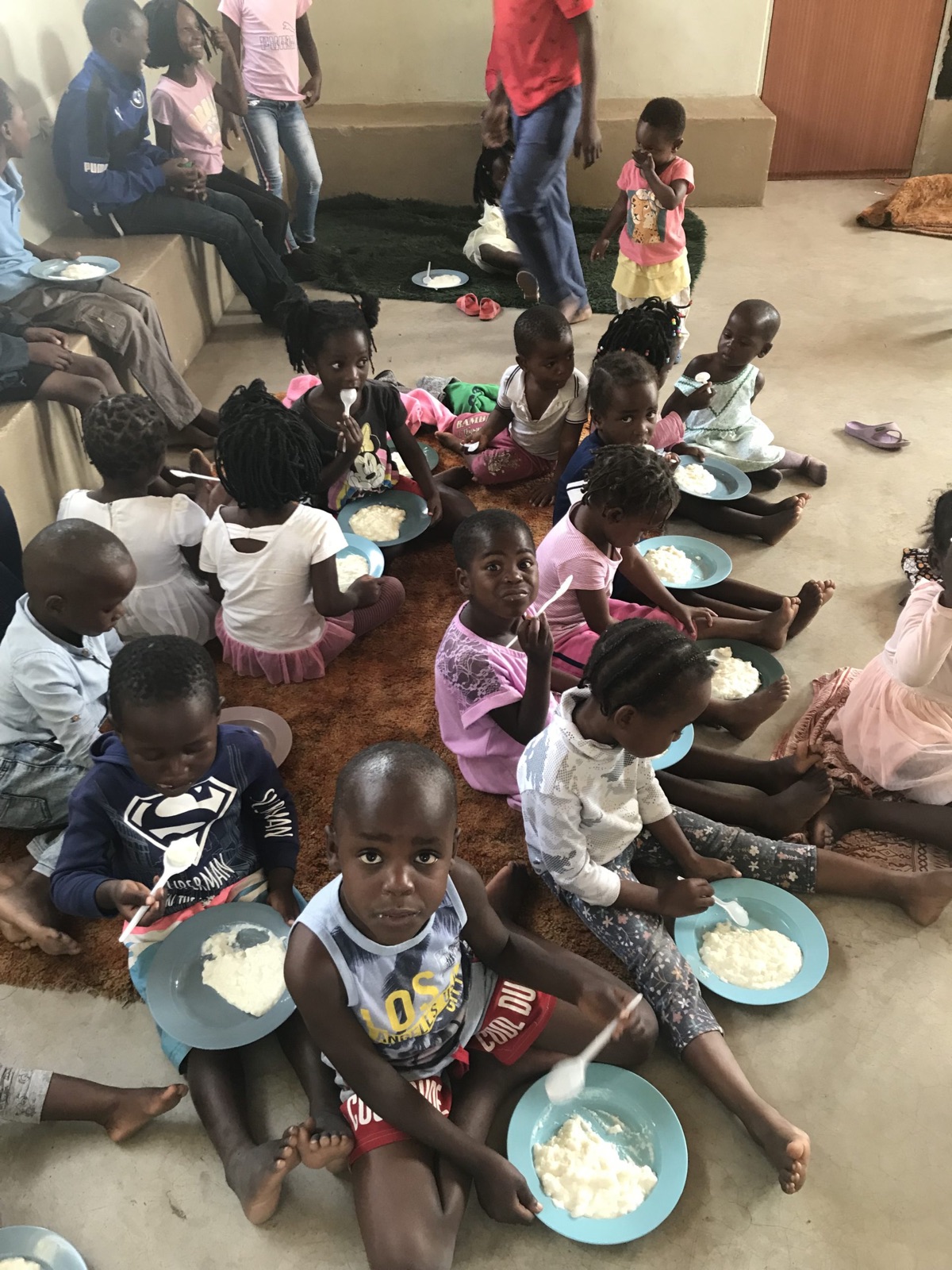 Kinder sitzen im Kinderhaus in Maresa auf dem Boden und essen von blauen Tellern